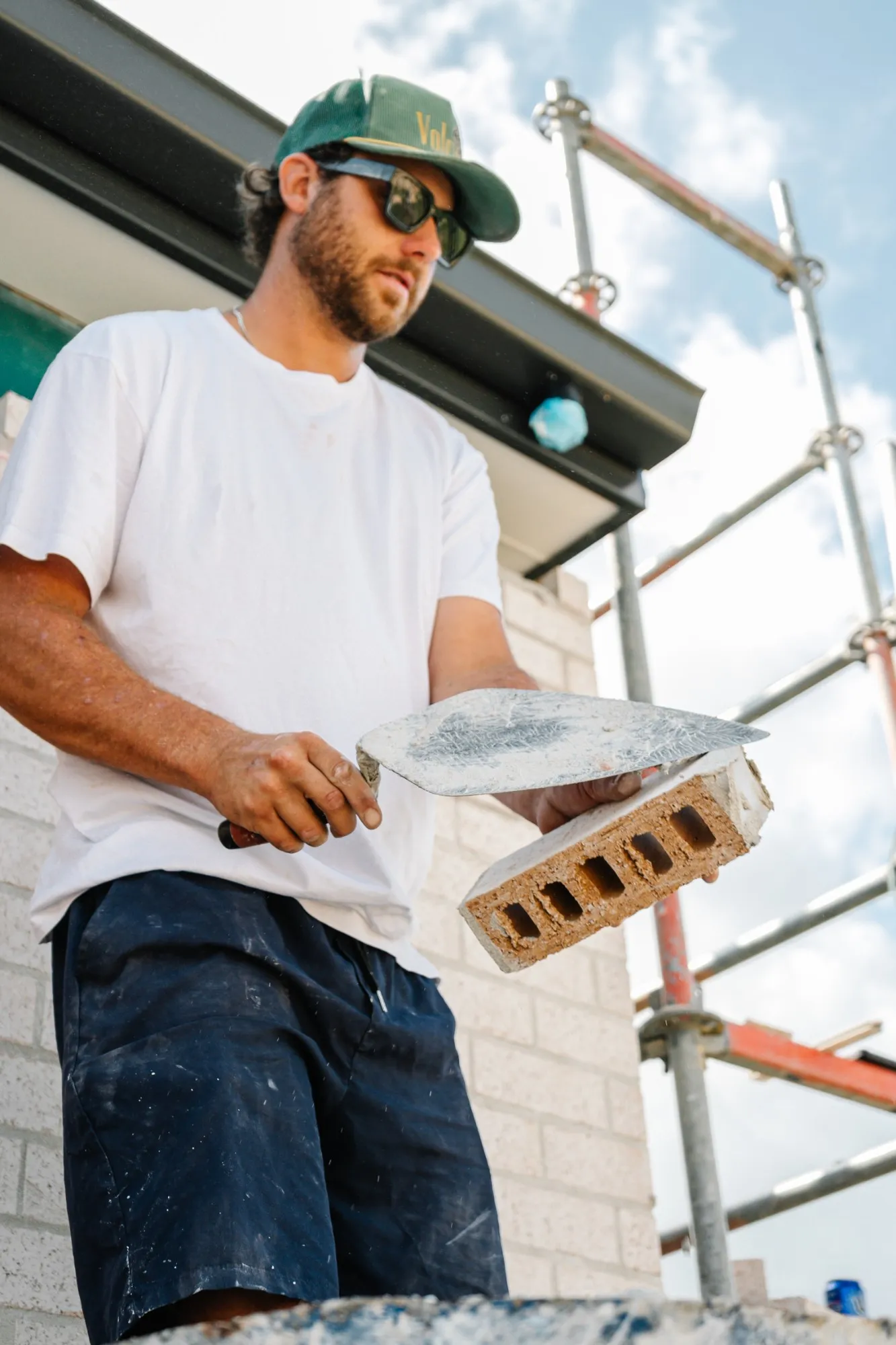 A bricklayer buttering a brick with mortar beside scaffolding on a new build
